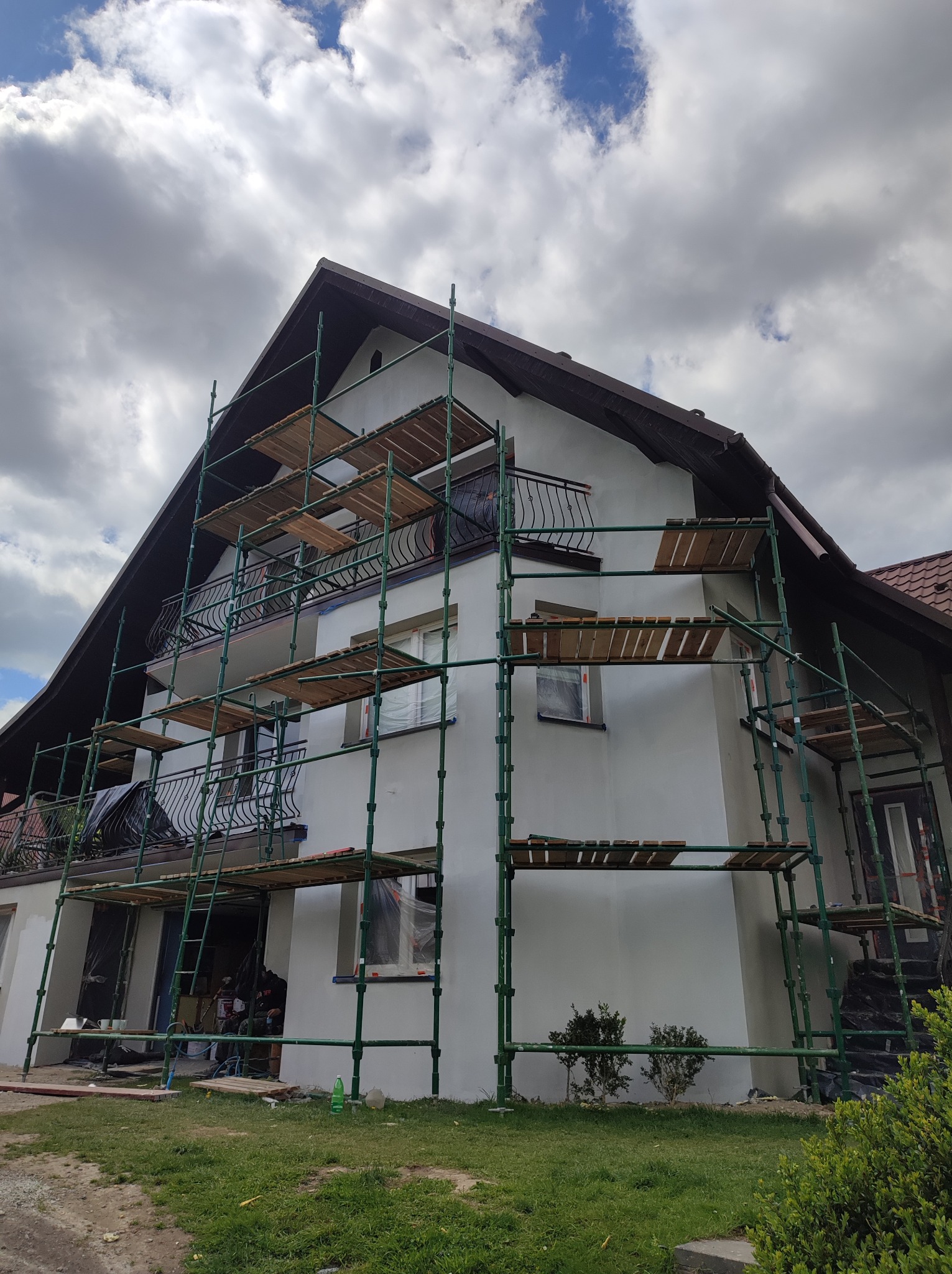 Dom w Ochotnicy Dolnej z rusztowaniem podczas prac elewacyjnych. Widoczne świeżo pomalowane ściany i przygotowane okna. Ujęcie z dołu, pochmurne niebo.