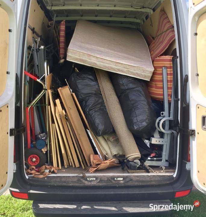 Wnętrze busa wypełnione meblami, dywanem w rolce i workami. Widok z tyłu pojazdu, otwarte drzwi. Przeprowadzka.