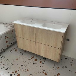 Meble na wymiar Wojciech Milewski - Nowoczesna łazienka z podwójną umywalką na szafce z jasnego drewna. Na podłodze płytki lastryko. Widoczny fragment wanny i drabina.