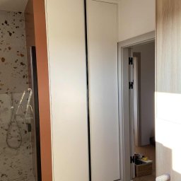 Meble na wymiar Wojciech Milewski - Biała szafa wnękowa z czarnymi uchwytami, w łazience z terazzo, widok na prysznic i otwarte drzwi do innego pomieszczenia. Szafa sięga od podłogi do sufitu.