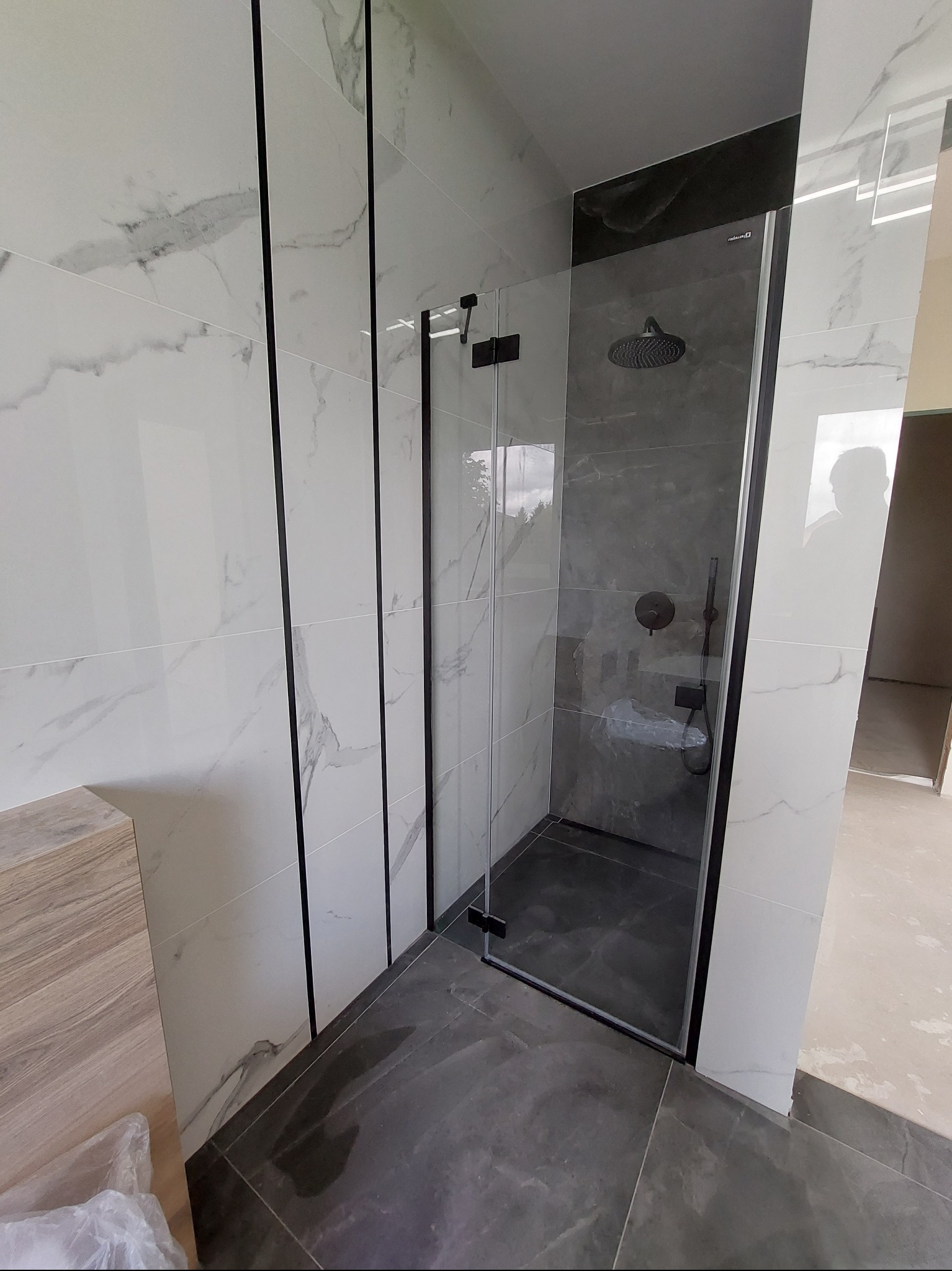 Nowoczesna kabina prysznicowa z czarnymi detalami i marmurowymi płytkami, szklane drzwi, ciemna podłoga, świeżo wykończona łazienka.