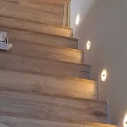 Drewniane schody z podświetleniem LED w ścianie, ciepłe światło, widoczne detale faktury drewna i subtelne oświetlenie.