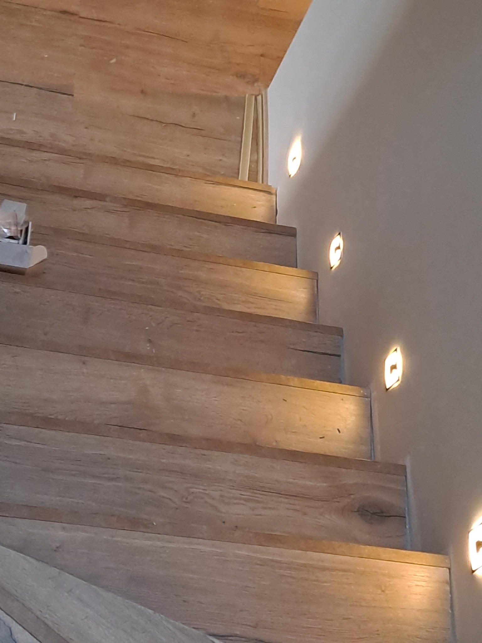 Drewniane schody z podświetleniem LED w ścianie, ciepłe światło, widoczne detale faktury drewna i subtelne oświetlenie.