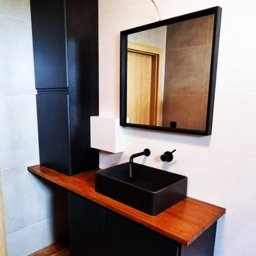 Meble Mnich - Nowoczesna łazienka w Goleszowie: czarna szafka pod umywalkę z drewnianym blatem, wysoka szafka i lustro w czarnej ramie. Minimalistyczny design, eleganckie wykończenie.