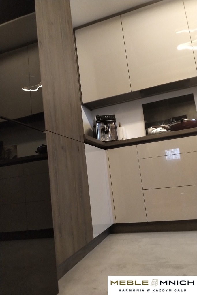 Nowoczesna kuchnia z beżowymi, lakierowanymi frontami i drewnopodobnymi bokami. Na blacie ekspres do kawy i płyta indukcyjna.