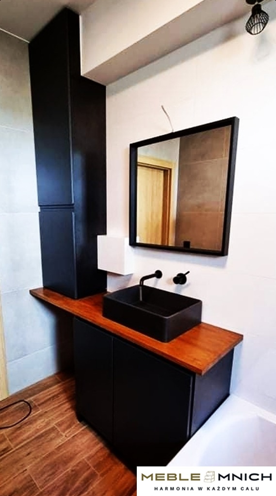 Nowoczesna łazienka w Goleszowie: czarna szafka pod umywalkę z drewnianym blatem, wysoka szafka i lustro w czarnej ramie. Minimalistyczny design, eleganckie wykończenie.