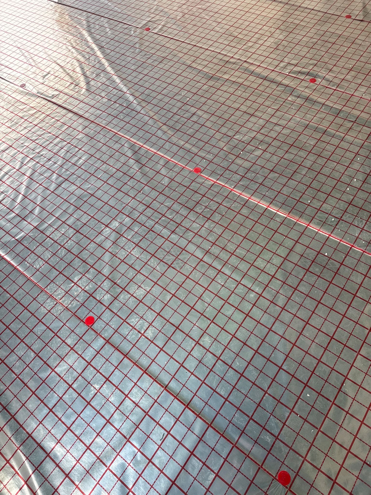 Mata grzewcza z czerwoną siatką i mocowaniami, przygotowana do instalacji ogrzewania podłogowego, widok z góry, jasne oświetlenie.