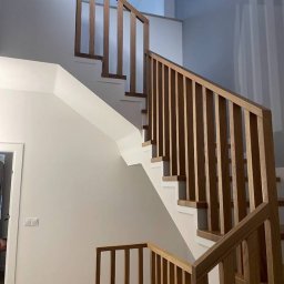 BEZPIECZNYWYKONAWCA.PL SPÓŁKA Z OGRANICZONĄ ODPOWIEDZIALNOŚCIĄ - Nowoczesne schody drewniane z jasnymi ścianami i minimalistyczną balustradą. Widok z dołu, podkreślający geometrię i detale wykończenia.