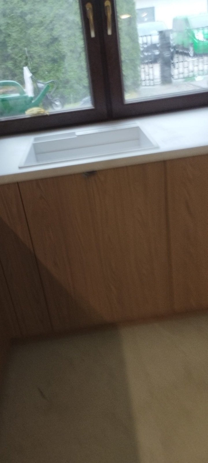 Nowoczesna szafka pod umywalkę z drewnianymi frontami i białym blatem, widok na okno z zielenią. Minimalistyczny design, jasne wnętrze.