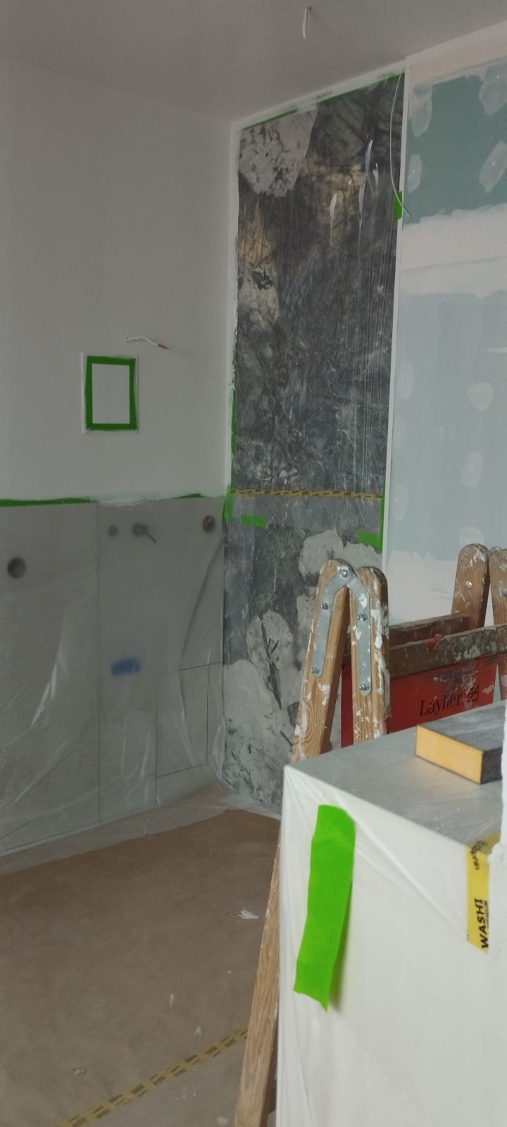 Łazienka w trakcie prac wykończeniowych: zabezpieczone folią ściany, fragment drabiny malarskiej, widoczne instalacje. Przygotowanie do dalszych prac.