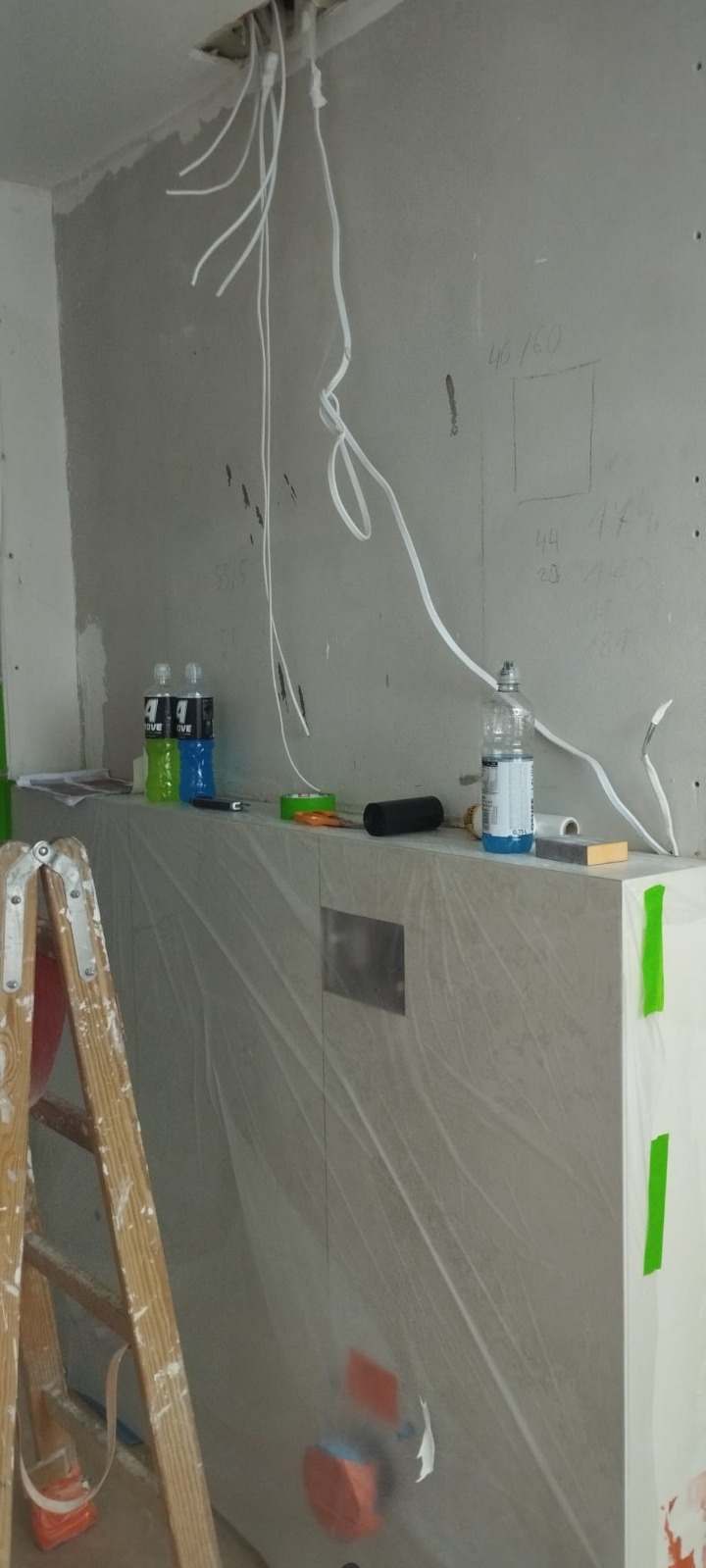 Instalacja elektryczna w łazience przed wykończeniem: przewody zwisają z sufitu, ściany przygotowane pod płytki, drabina malarska w rogu. Widoczne narzędzia i materiały.