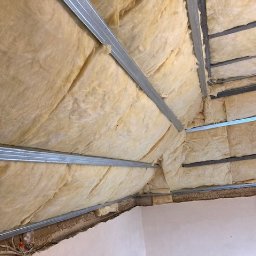 Usługi budowlane KF - Ocieplone poddasze z widoczną wełną mineralną i metalową konstrukcją. Ukończony etap prac izolacyjnych w budynku. Widok z dołu.