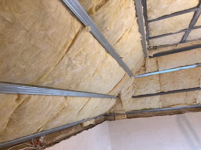 Ocieplone poddasze z widoczną wełną mineralną i metalową konstrukcją. Ukończony etap prac izolacyjnych w budynku. Widok z dołu.