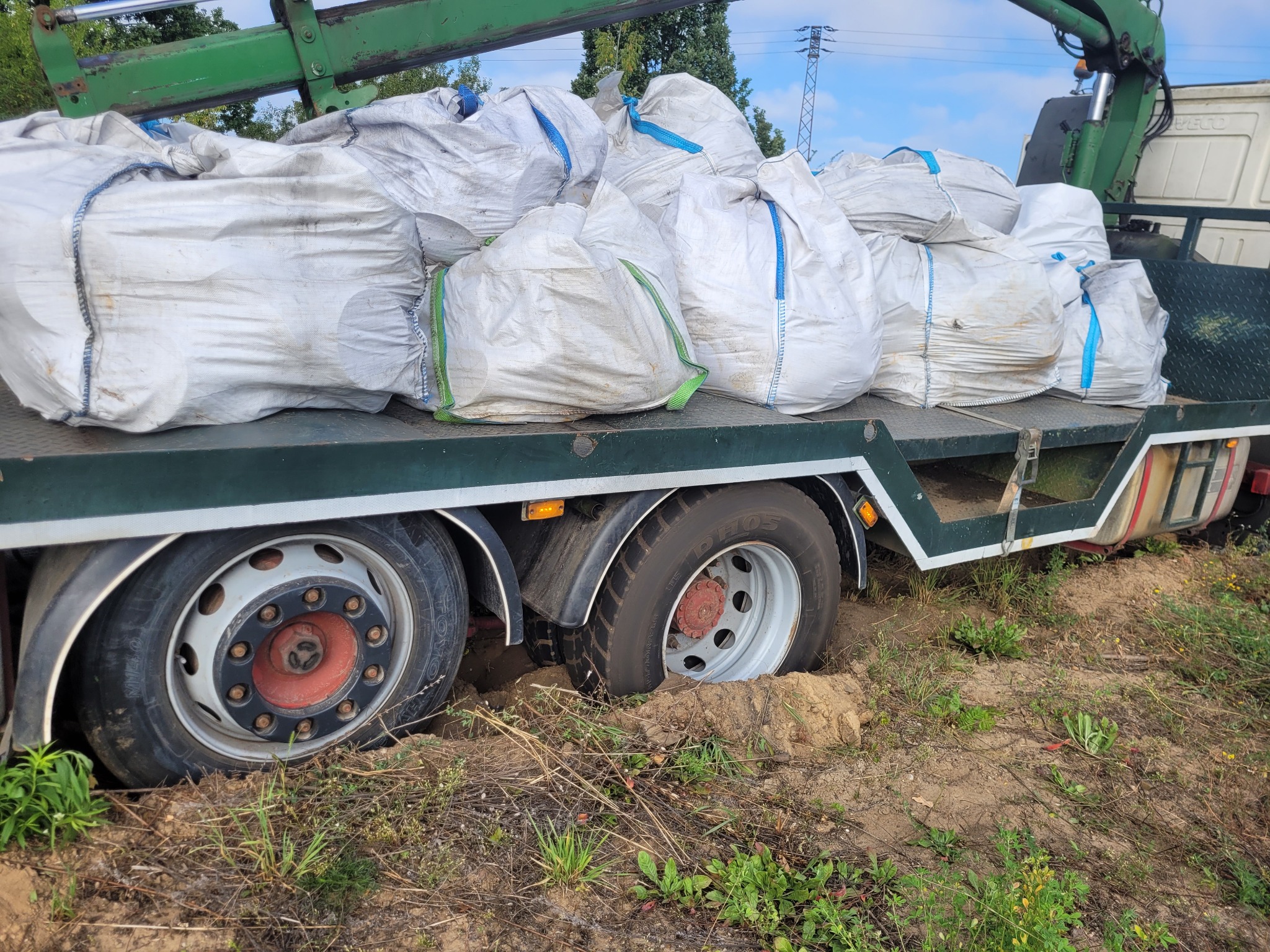 Ciężarówka z załadunkiem w grząskim terenie, Latowicz. Koła zapadły się w ziemi. Widoczny fragment dźwigu i worki zabezpieczone pasami na platformie.