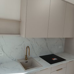 Meblarium Marcin Hałas - Jasna kuchnia na wymiar z marmurowym blatem, złotą baterią i płytą indukcyjną. Minimalistyczny design, gładkie fronty szafek i subtelne uchwyty.