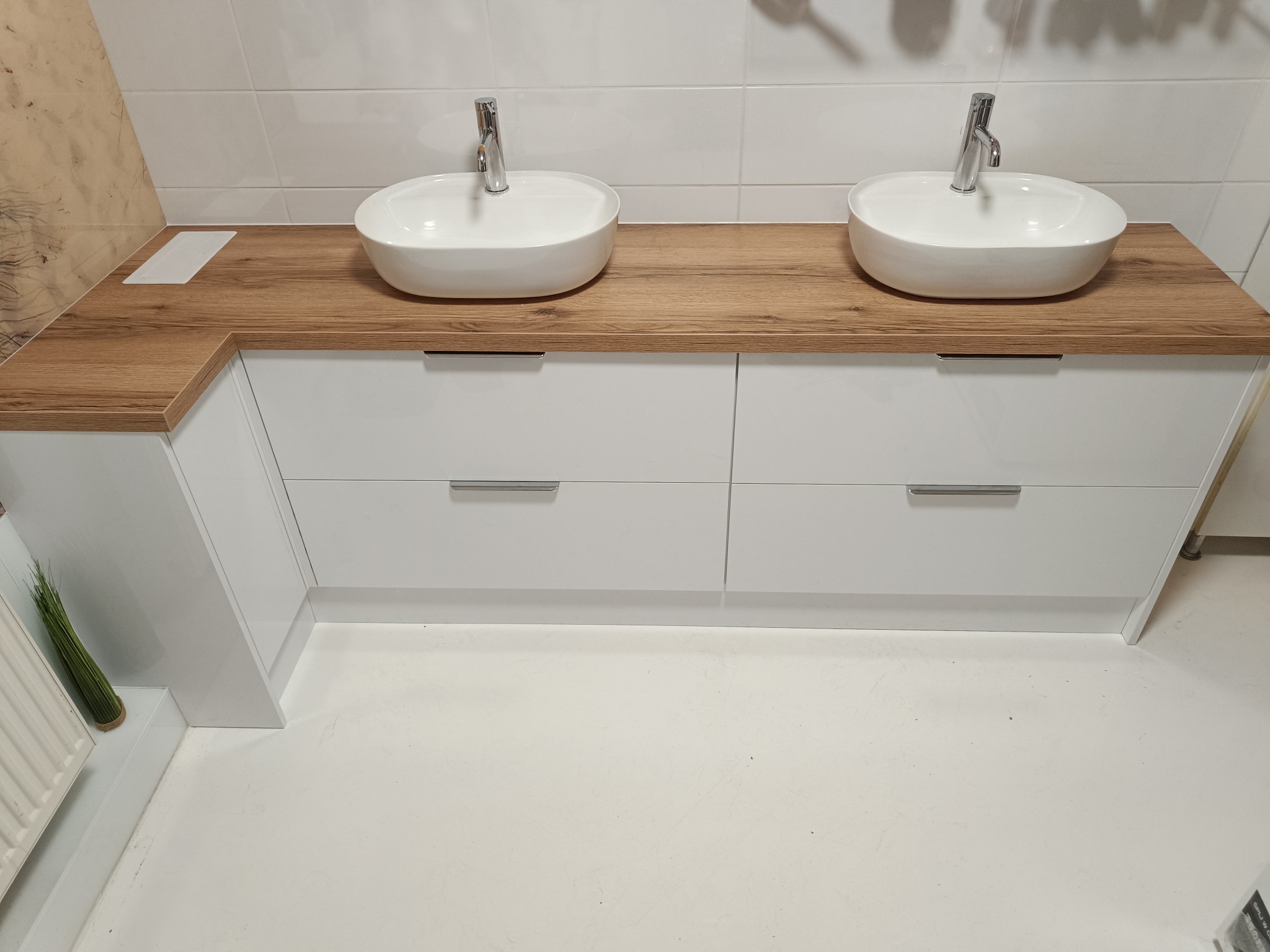 Nowoczesna szafka łazienkowa z dwoma umywalkami nablatowymi. Białe fronty szafek i blat z drewnopodobnym dekorem. Minimalistyczny design, jasne wnętrze.