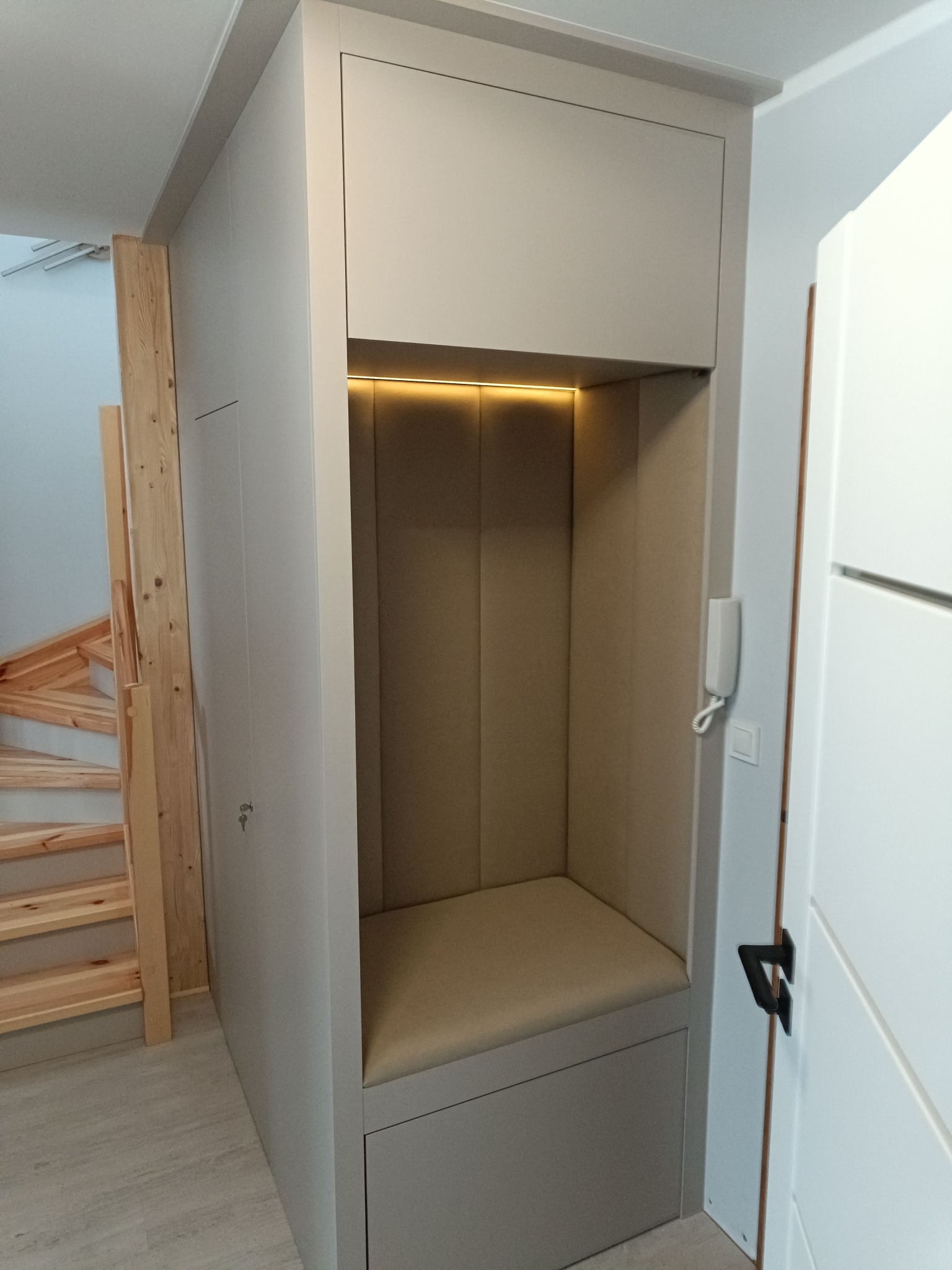 Funkcjonalna zabudowa wnęki z siedziskiem i oświetleniem LED, dopasowana do schodów z jasnego drewna. Minimalistyczny design, jasna kolorystyka.