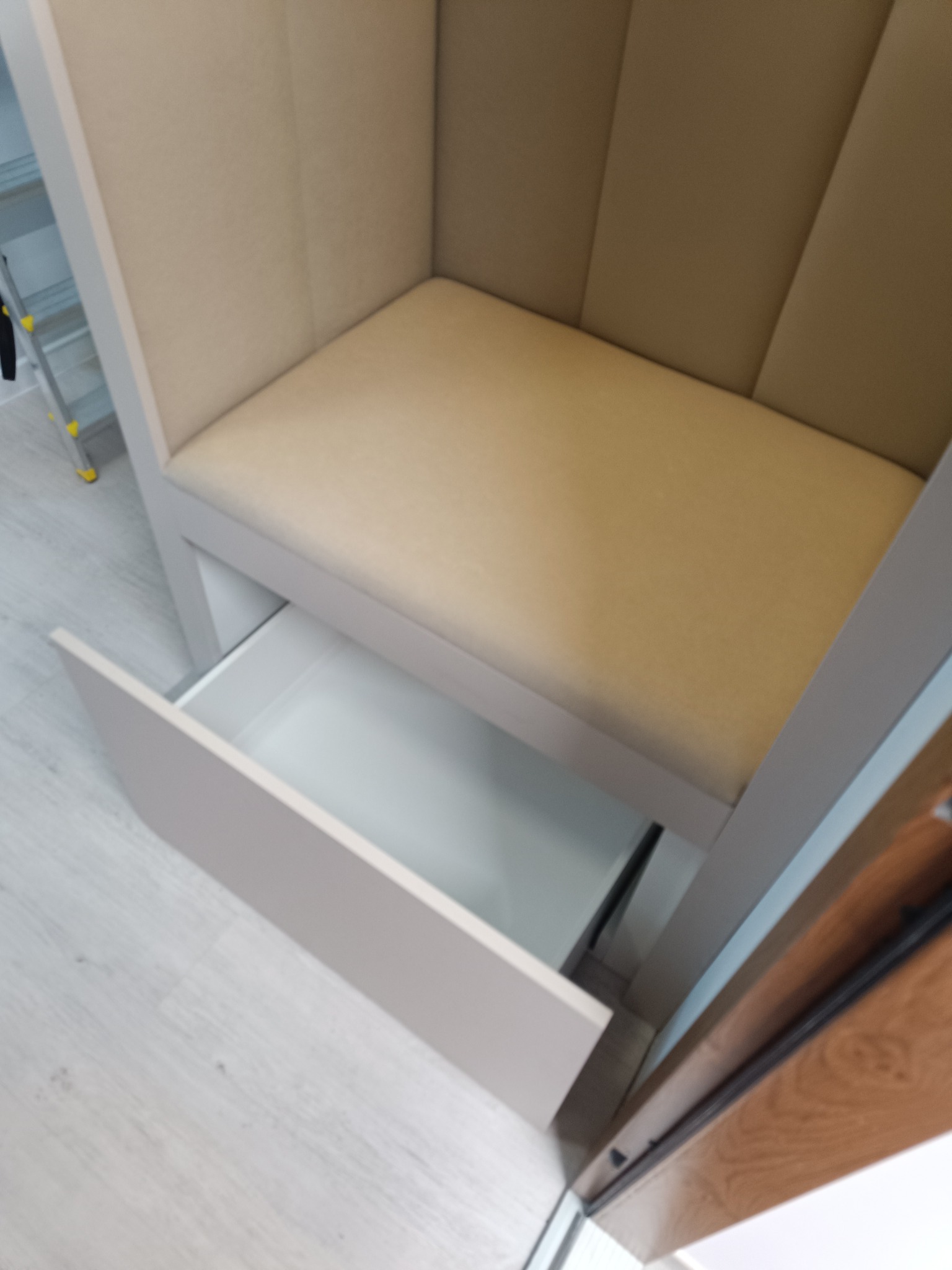 Beżowa szafa wnękowa z wysuwaną szufladą, widok z góry. Tapicerowane siedzisko i jasne wykończenie. Minimalistyczny design, nowoczesne wnętrze.