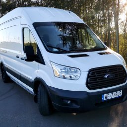 TRIOTRANS Paweł Czuba - Biały Ford Transit z polską rejestracją WE-778UG, zaparkowany na asfalcie, z drzewami w tle i promieniami słońca. Widok z przodu, lekko z boku.