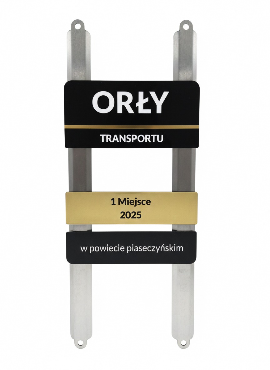 Tablica z napisem 'Orły Transportu', informująca o zajęciu 1 miejsca w 2025 roku w powiecie piaseczyńskim. Metalowa konstrukcja, czarno-złote tabliczki.