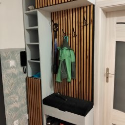 Łukasz Skorupski - Funkcjonalna zabudowa przedpokoju z drewnianymi lamelami, szafką na buty z siedziskiem i wieszakami na ubrania. Nowoczesny design, szara kolorystyka.