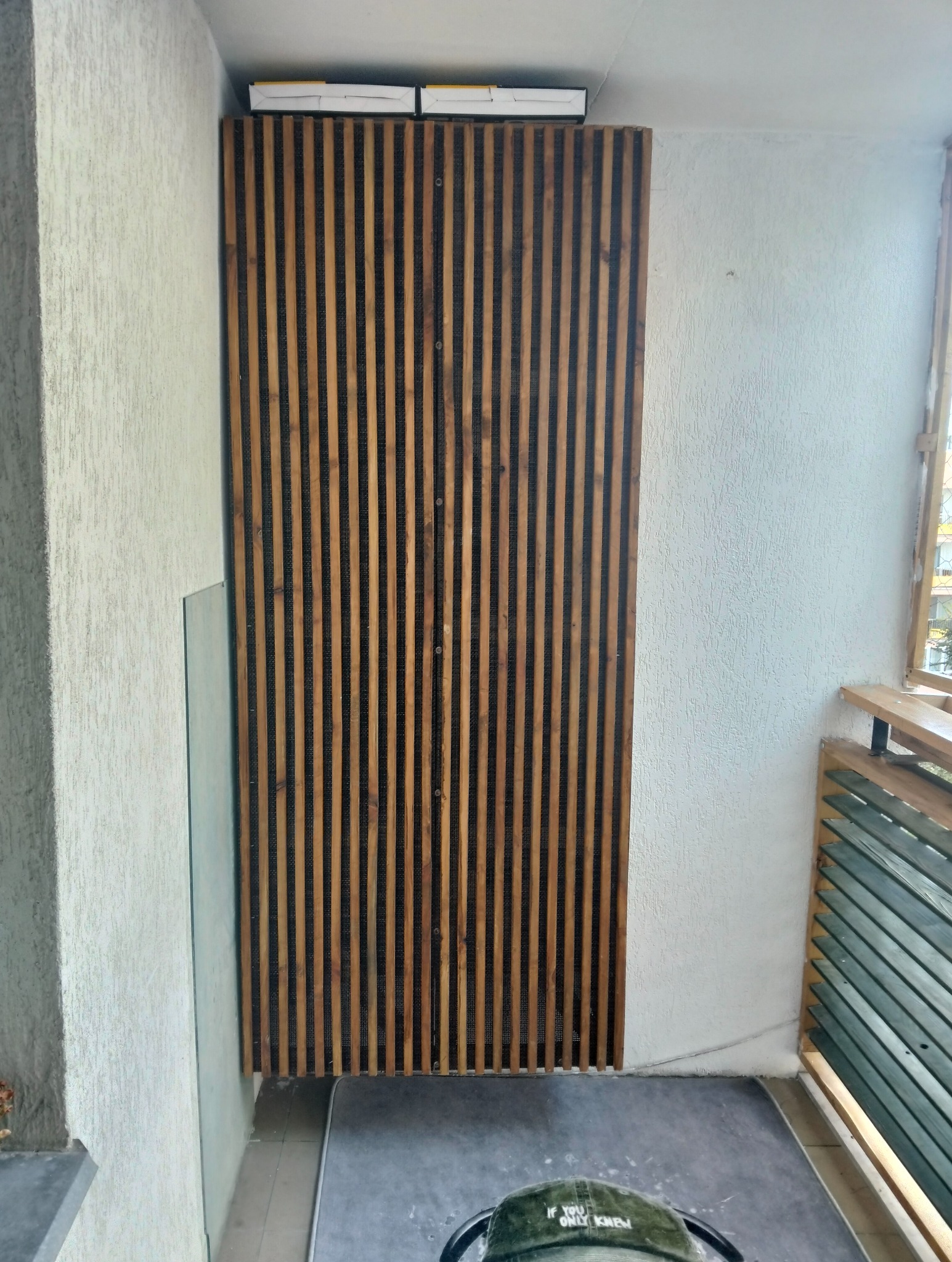 Drewniana ścianka działowa z pionowych listew na balkonie, z widoczną fakturą ściany i elementami balustrady. Ujęcie z dołu, podkreślające wysokość konstrukcji.