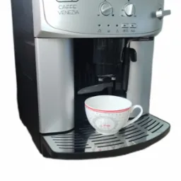 Szaro-czarny ekspres DeLonghi Caffe Venezia z filiżanką na ociekaczu. Widoczne pokrętła regulacji i ikony funkcji. Górna część obudowy srebrna, bok czarny.