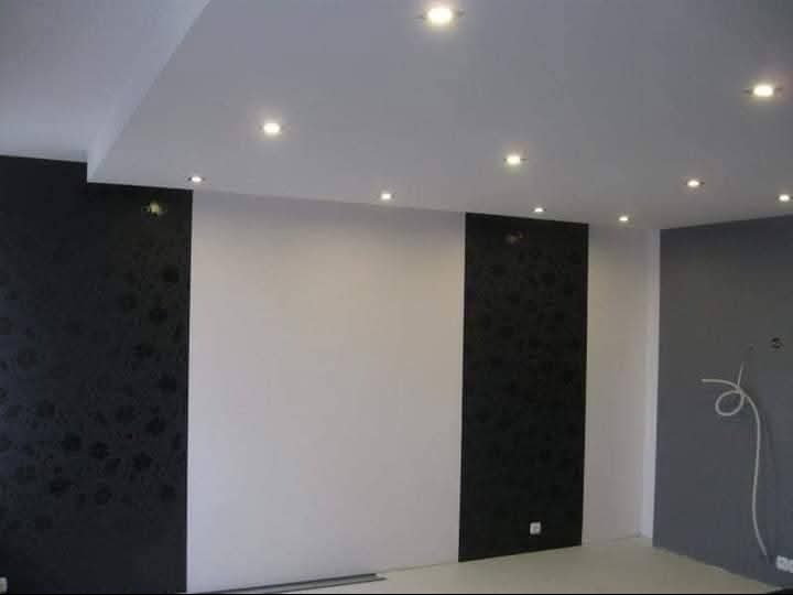 Wykończone wnętrze pokoju z białymi i czarnymi panelami dekoracyjnymi na ścianach oraz oświetleniem punktowym na suficie. Widoczne gniazdka elektryczne.
