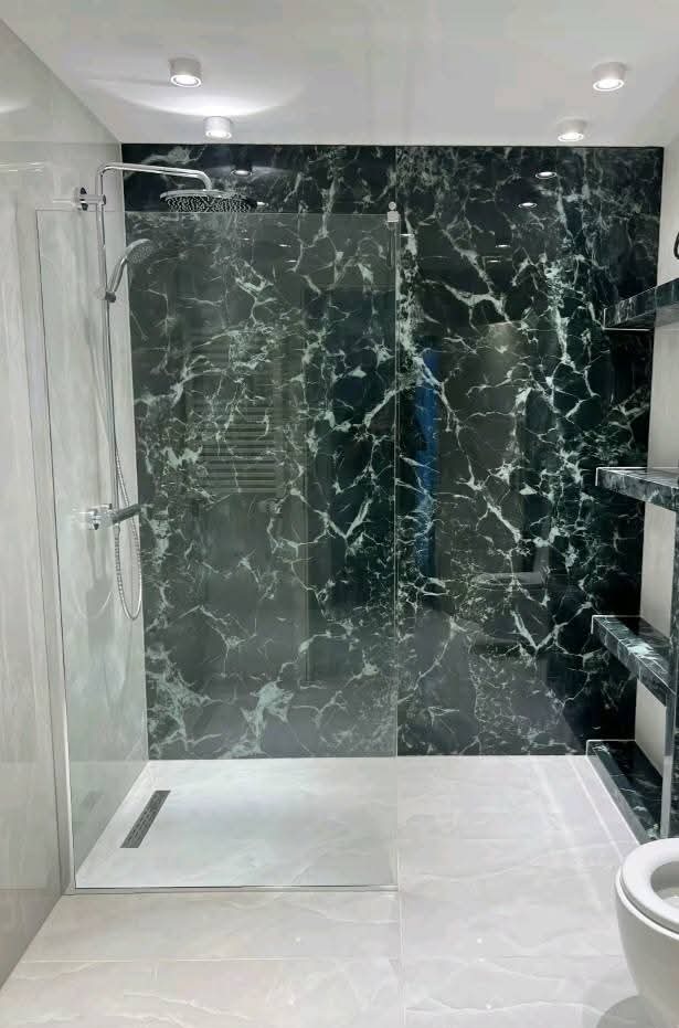 Nowoczesna kabina prysznicowa z marmurową ścianą i szklanymi drzwiami, minimalistyczny design, jasne oświetlenie sufitowe, widoczny odpływ liniowy.