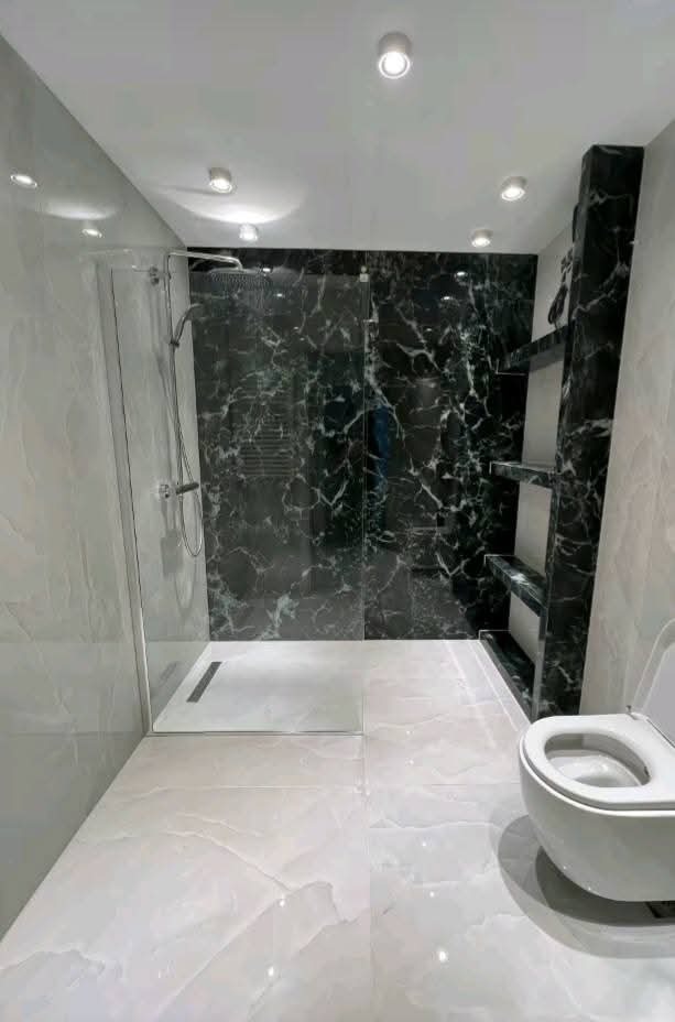Nowoczesna łazienka z kabiną prysznicową typu walk-in, marmurowymi płytkami w odcieniach szarości i czerni oraz podświetleniem sufitowym.