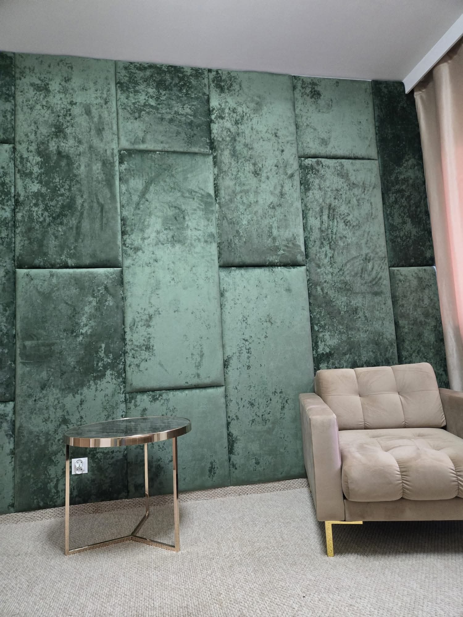Panel ścienny z zielonego weluru z efektem patyny za beżowym fotelem i złotym stolikiem kawowym na tle jasnego dywanu. Nowoczesny design wnętrza.