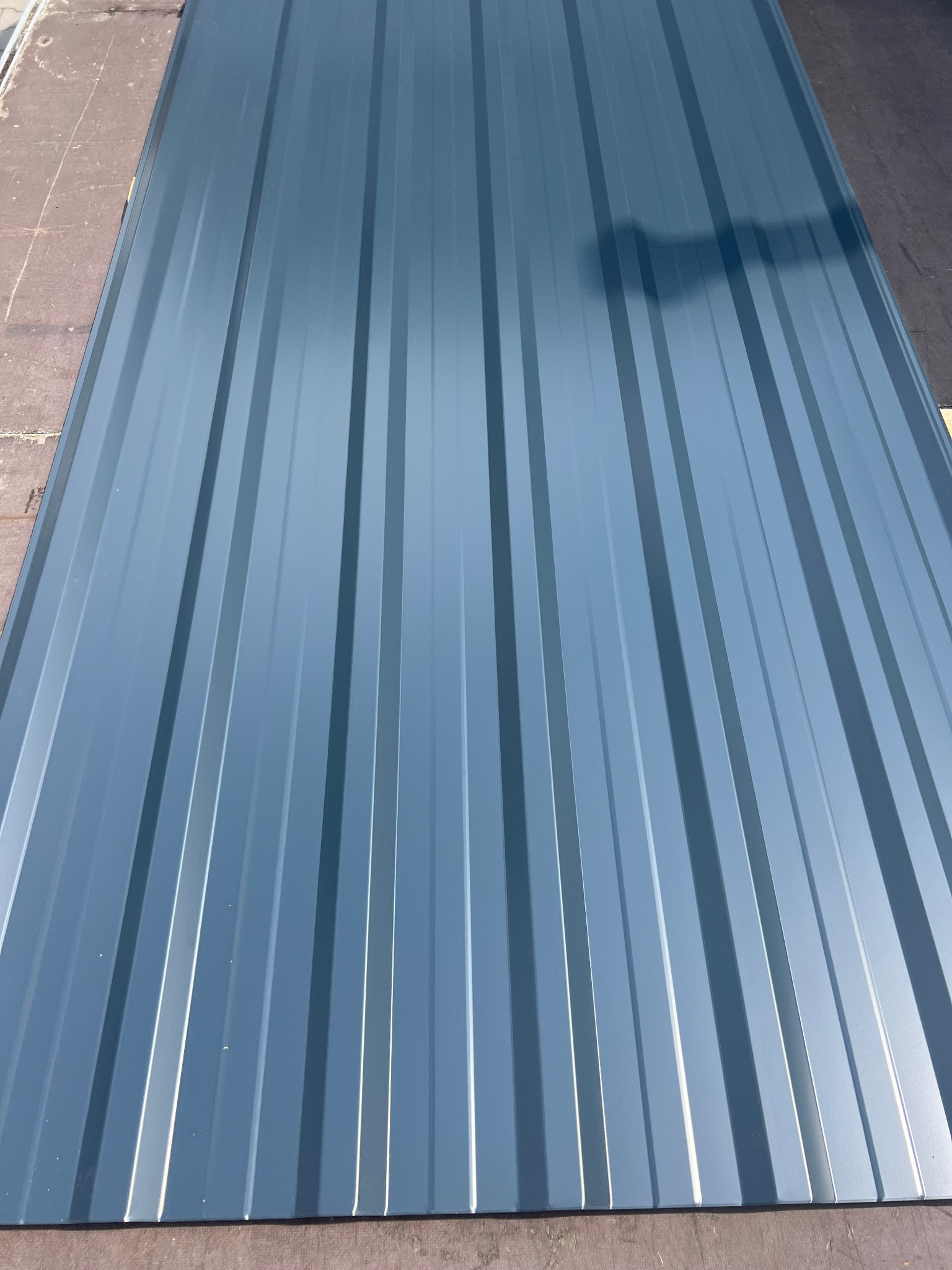 Szara blacha trapezowa z wyraźnym cieniowaniem, ułożona na drewnianym podłożu, widok z góry, podkreślający symetrię i regularność profilu.