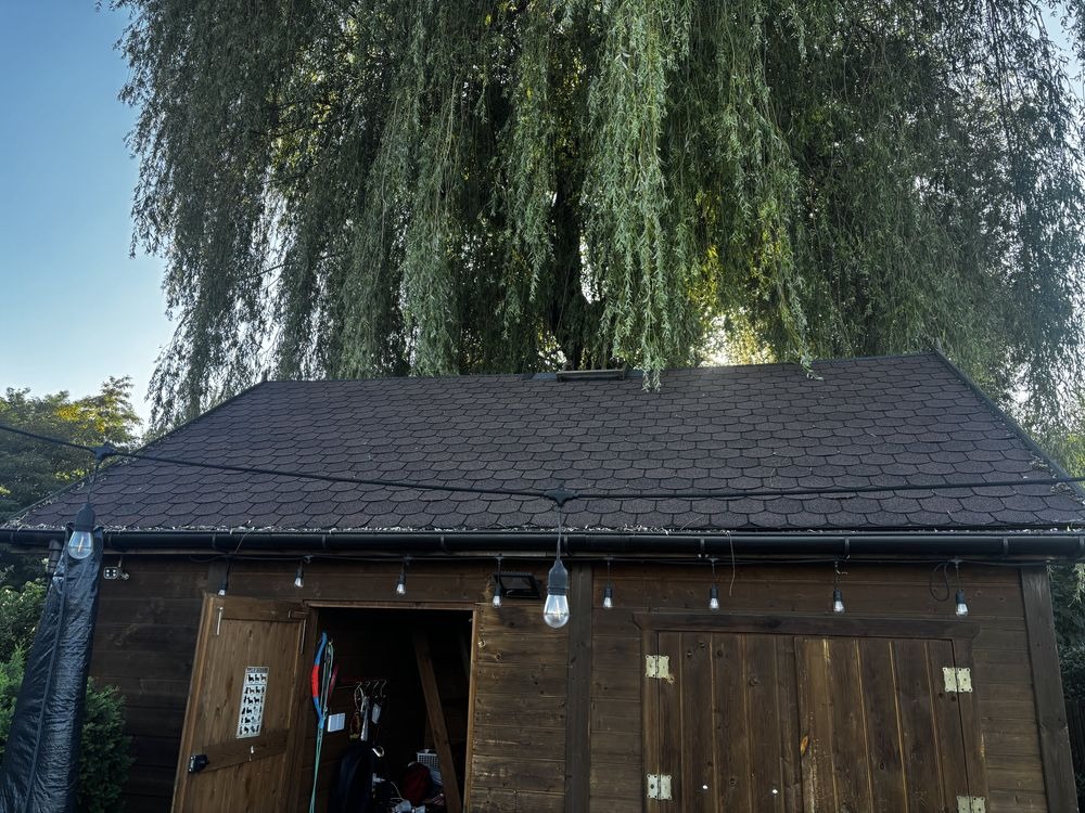 Dach pokryty brązową dachówką bitumiczną na drewnianym budynku w Grojcu, widok przed renowacją. Dekoracyjne lampki dodają uroku.