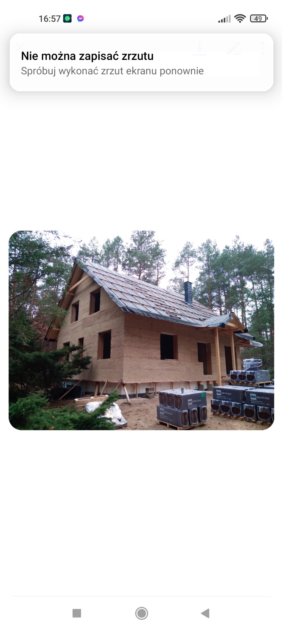 Surowy dom z gliny w lesie na etapie budowy, z widocznym dachem pokrytym folią i paletami z materiałami budowlanymi. Widoczne ściany z gliny.