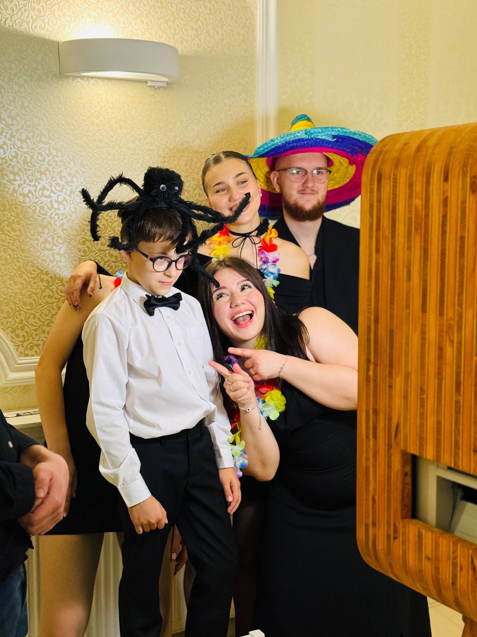 Uśmiechnięta grupa osób w przebraniach pozuje do zdjęcia przy fotobudce. Wesoła atmosfera, różnorodne rekwizyty, jasne oświetlenie. Dekoracyjne tło.