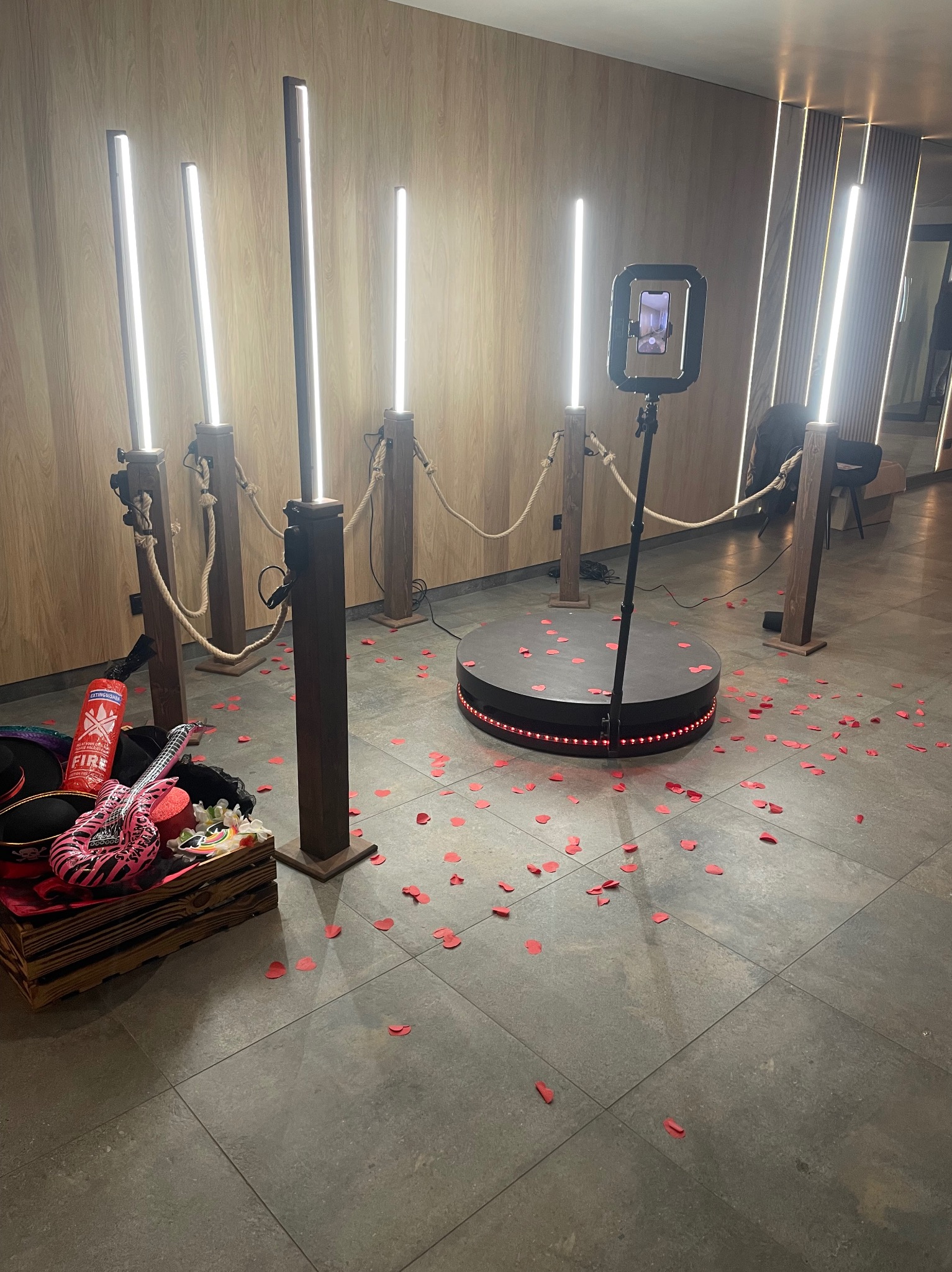 Nowoczesna fotobudka 360° z rekwizytami (gitara, kapelusz) i rozsypanymi czerwonymi sercami. Oświetlenie LED tworzy imprezowy klimat.