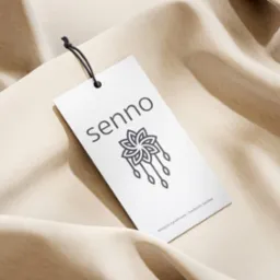 Elegancja w detalu: Metka z logo 'senno' z motywem kwiatowym na tle beżowej tkaniny. Minimalistyczny design dla tekstyliów sypialnianych, podkreślający subtelność marki.