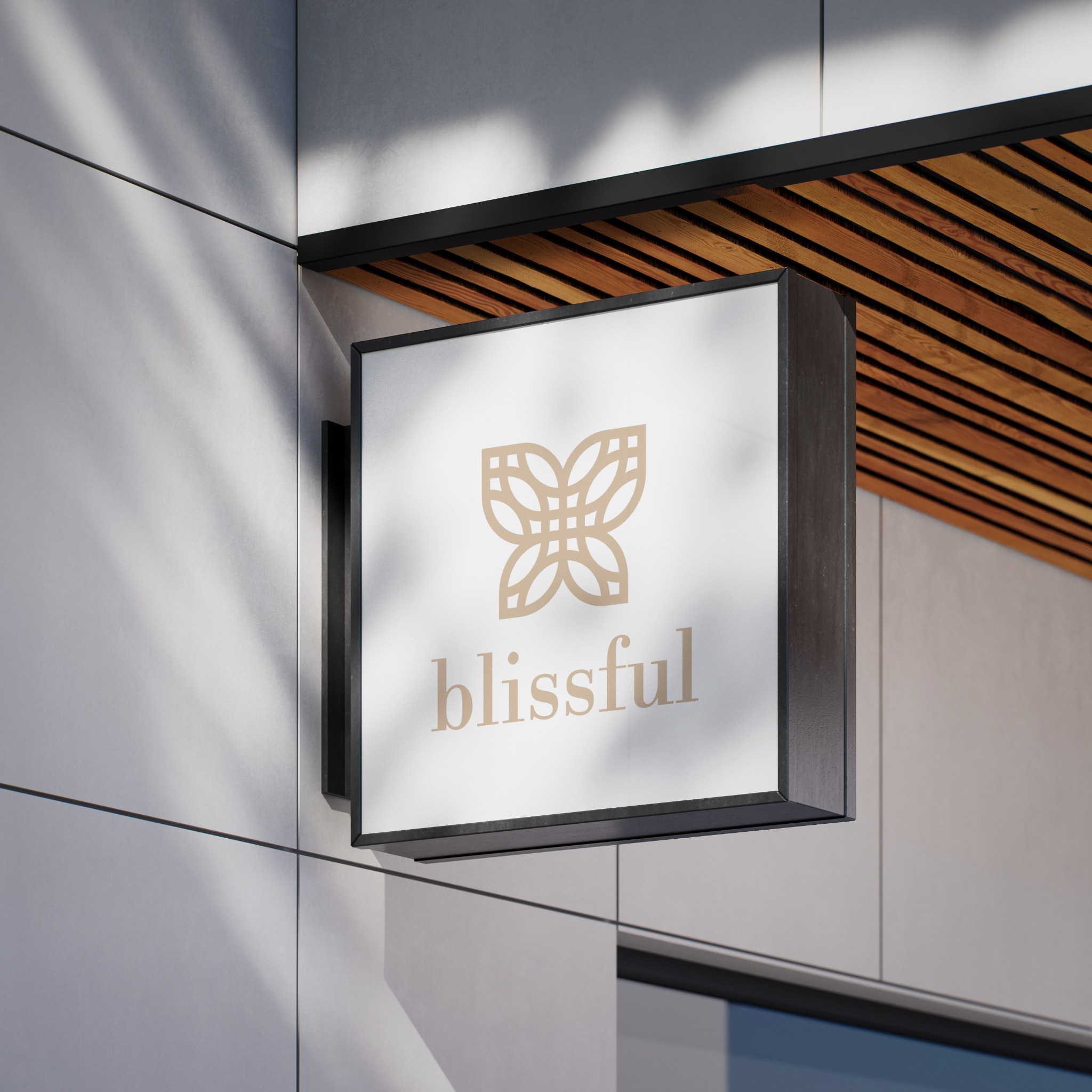 Kwadratowy szyld z logo 'blissful' na fasadzie budynku, oświetlony naturalnym światłem z cieniem liści. Szyld w kolorach beżu i bieli, z drewnianym elementem nad nim.