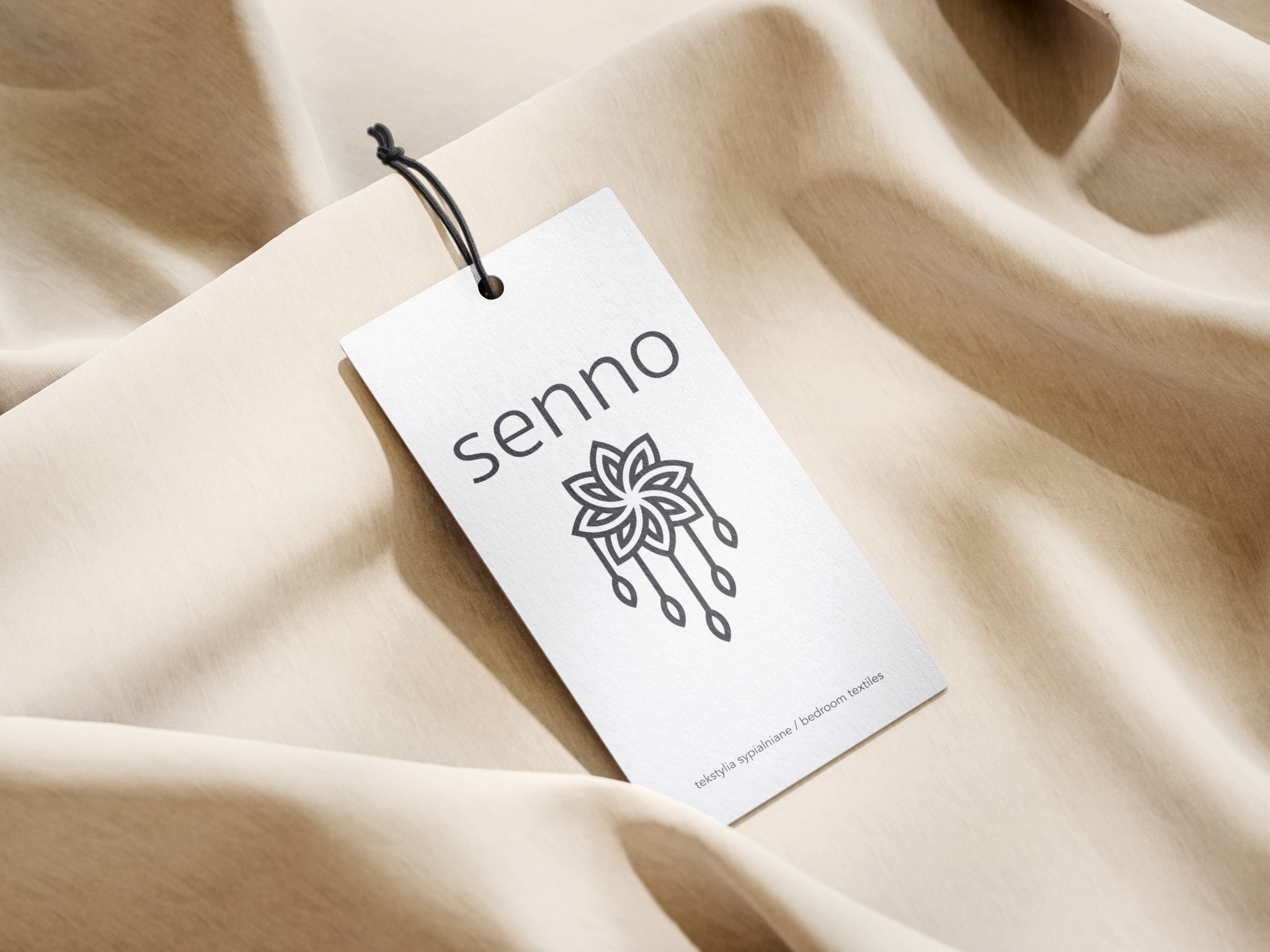 Elegancja w detalu: Metka z logo 'senno' z motywem kwiatowym na tle beżowej tkaniny. Minimalistyczny design dla tekstyliów sypialnianych, podkreślający subtelność marki.