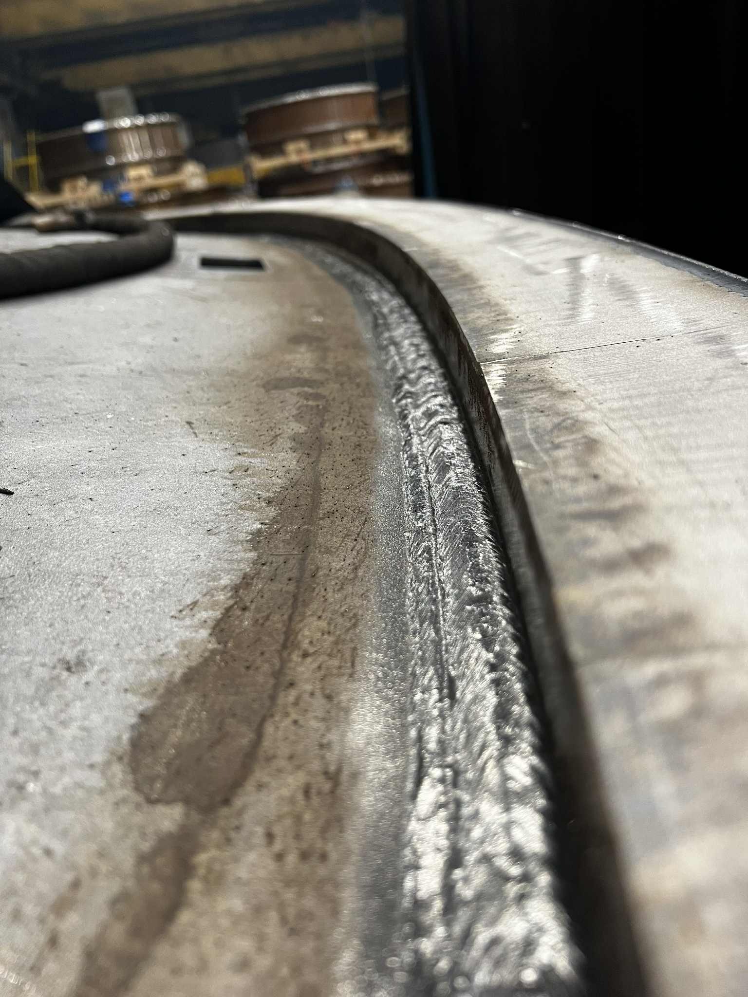 Detal spoiny na okrągłym elemencie metalowym, widoczne ślady obróbki i wilgoć, surowe oświetlenie przemysłowe, perspektywa z bliska.