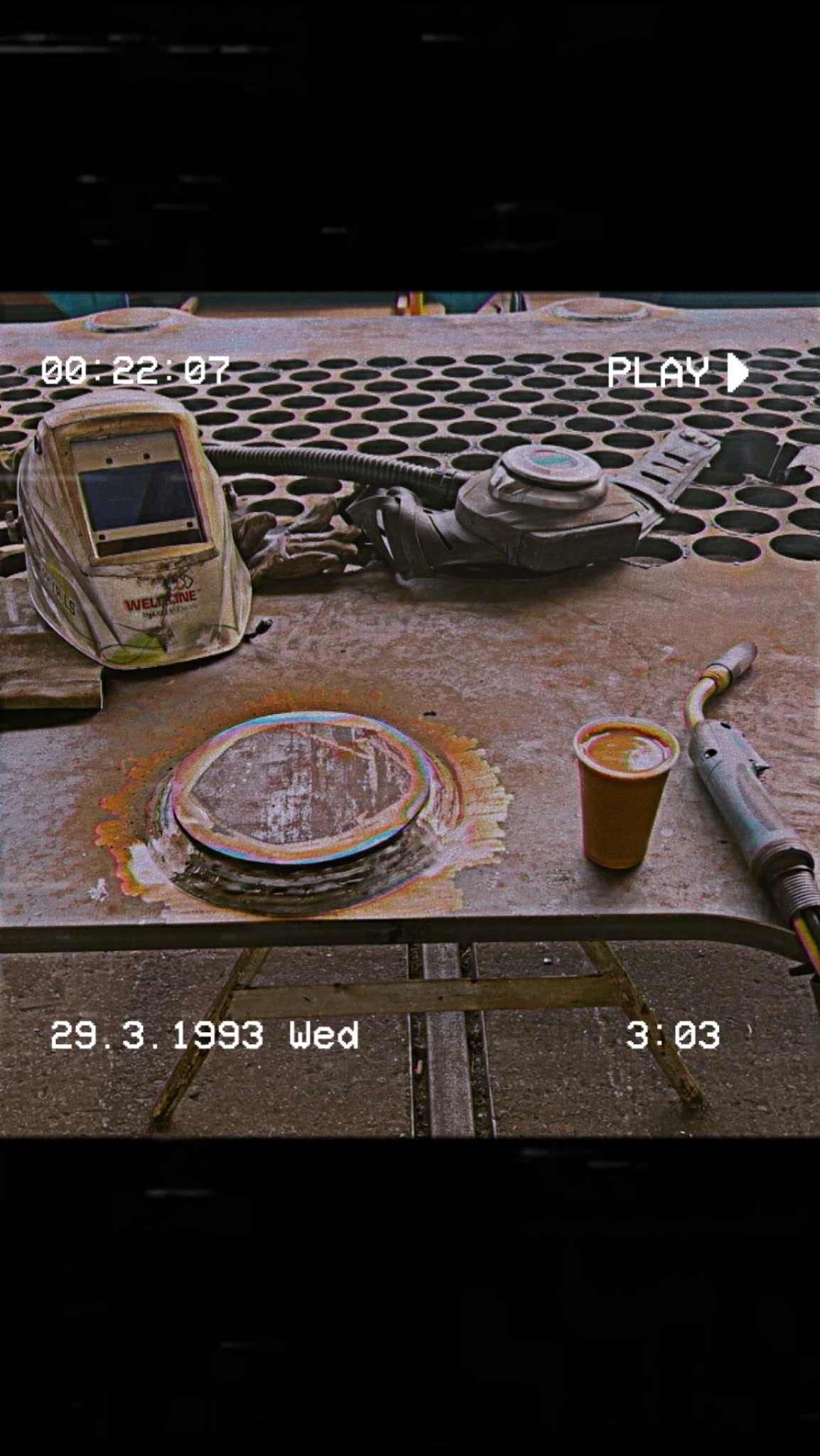 Stół warsztatowy z maską, uchwytem spawalniczym i kubkiem kawy obok spawu na metalu. Zdjęcie w stylu retro z datą 29.3.1993.