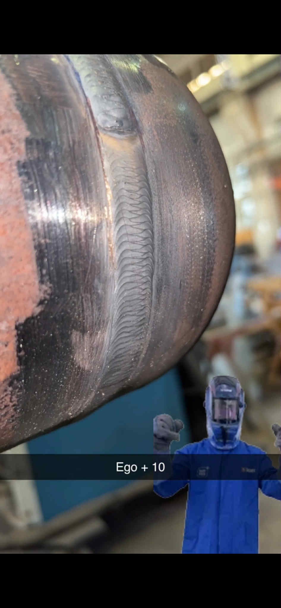 Precyzyjne spawy na metalowej rurze, widoczny wzór spoiny. W tle postać w kombinezonie i masce ochronnej.