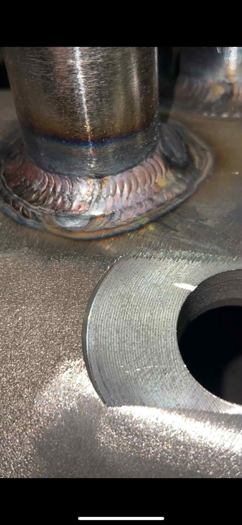 Szlifowana, metalowa konstrukcja po spawaniu z widocznymi, precyzyjnymi ściegami i otworem. Detal obróbki metalu z bliska, z charakterystycznym połyskiem.