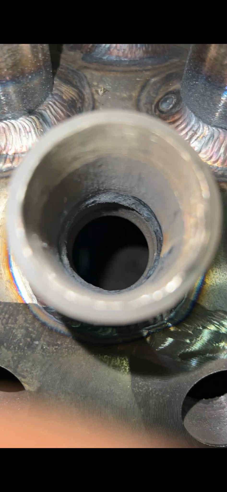 Spoina rury z widocznymi śladami spawania, tęczowe zabarwienie metalu. Widok z góry w otwór rury, ukazujący wnętrze połączenia.