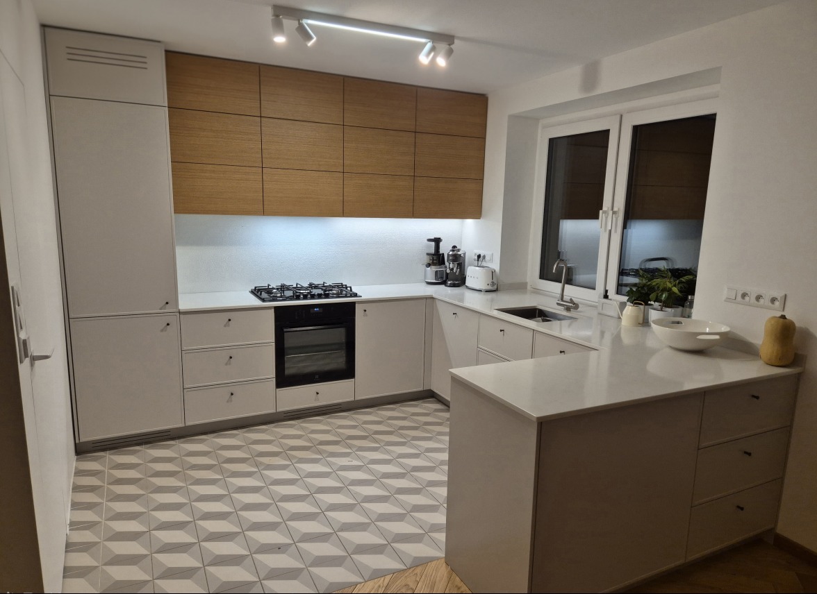 Nowoczesna kuchnia z białymi szafkami i drewnianymi górnymi frontami. Geometryczna podłoga i oświetlenie punktowe dodają charakteru.