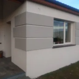 Wykończona elewacja domu jednorodzinnego z dekoracyjnymi, szarymi elementami w formie prostokątów wokół okna i na rogu budynku. Widoczny fragment wejścia i okna.