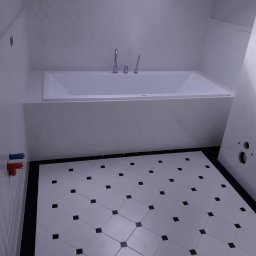 FIRMA BUDOWLANA MATEUSZ GRONOWICZ - Minimalistyczna łazienka z białą wanną i wzorzystą podłogą w romby z czarnymi akcentami. Widoczne przyłącza wodne i fragment instalacji.