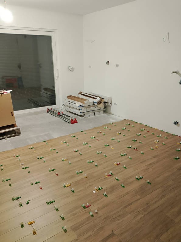 Układanie płytek podłogowych w Glinno, z użyciem systemu poziomowania. W tle widoczne paczki płytek i narzędzia.