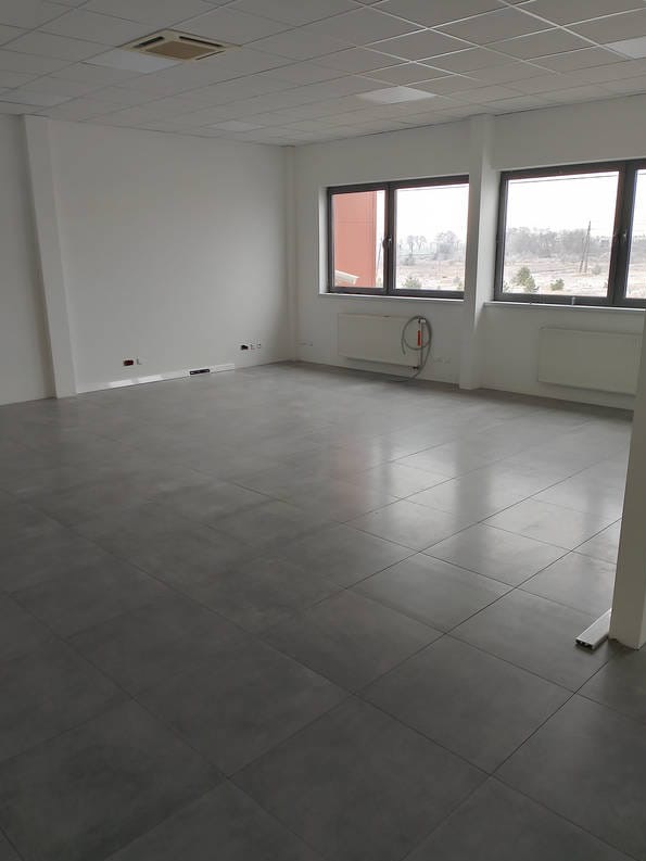 Wnętrze biura po malowaniu: szare płytki podłogowe, białe ściany, dwa okna z grzejnikami pod spodem, sufit kasetonowy z kratką wentylacyjną.