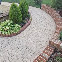 Kam-Dach Kamil Parczewski - Kaskadowa ścieżka z kostki brukowej w ogrodzie, obrzeża z cegły i roślin, krzesło ogrodowe w tle, widok z góry.